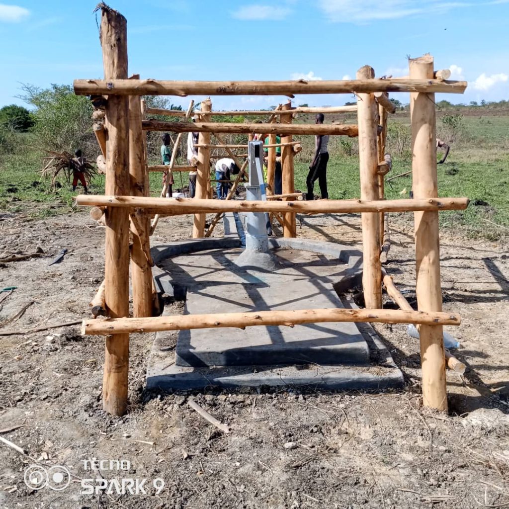 Workers installing a hand pump inside a timber enclosure in a rural field